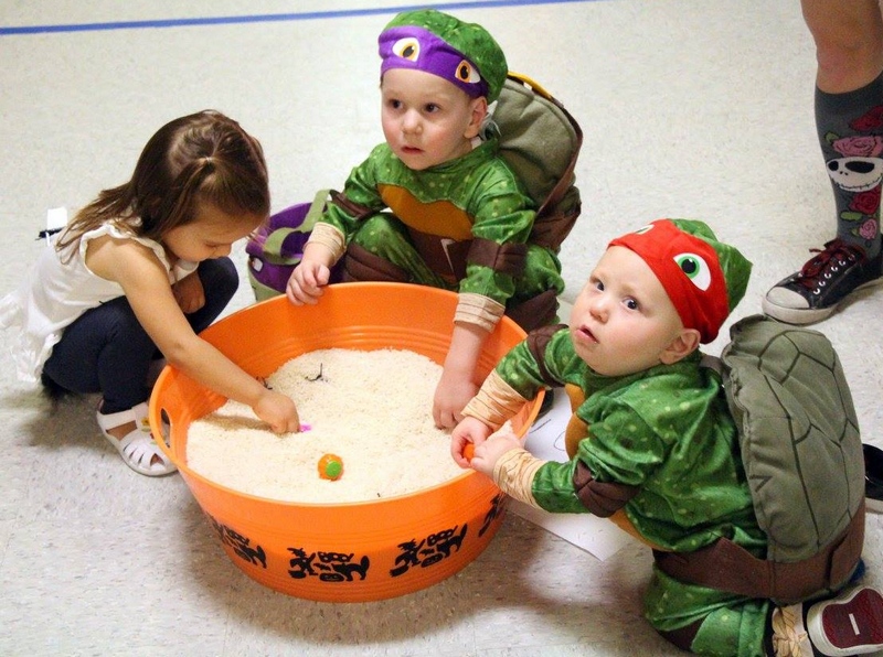 Three children playing in a giant bowl of rice. Two of the children are dressed in ninja turtle costumes.